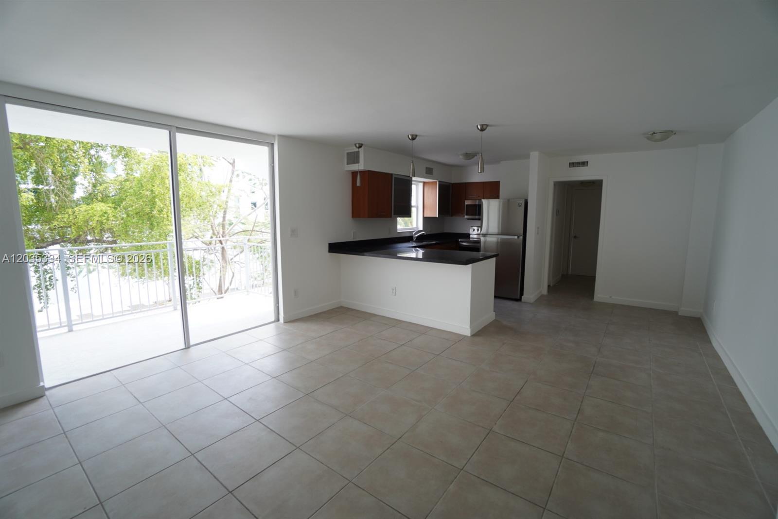 An open-concept kitchen with dark cabinets and a balcony view through sliding glass doors — 680 NE 64th St # A302, Miami FL 33138, MIAMI, FL