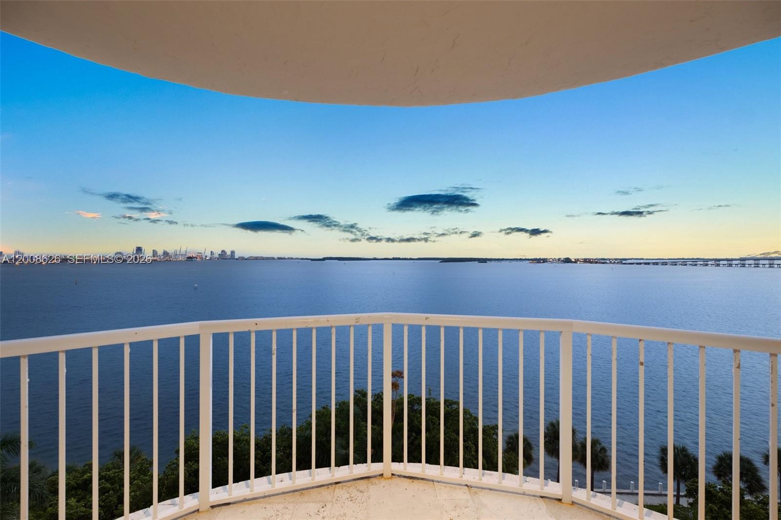 A balcony with a white railing overlooks a large body of water at sunset — 1420 Brickell Bay Dr # 1001A, Miami FL 33131, MIAMI, FL