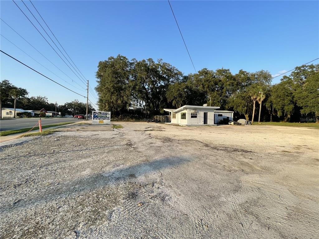 A gravel lot features a small white building and a sign near a paved road — 830 S MAIN STREET, WILDWOOD, FL