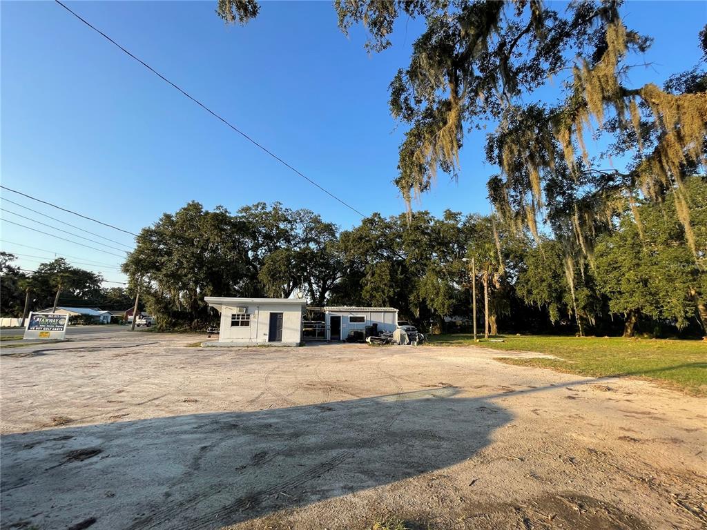 A small white commercial building sits on a large, unpaved gravel lot with mature trees — 830 S MAIN STREET, WILDWOOD, FL