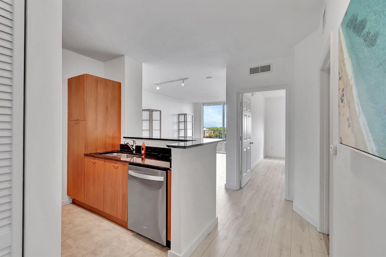 A kitchen with wood cabinets and a stainless steel dishwasher opens to a living area — 100 NE 6th Street # 505, Boynton Beach FL 33435, BOYNTON BEACH, FL