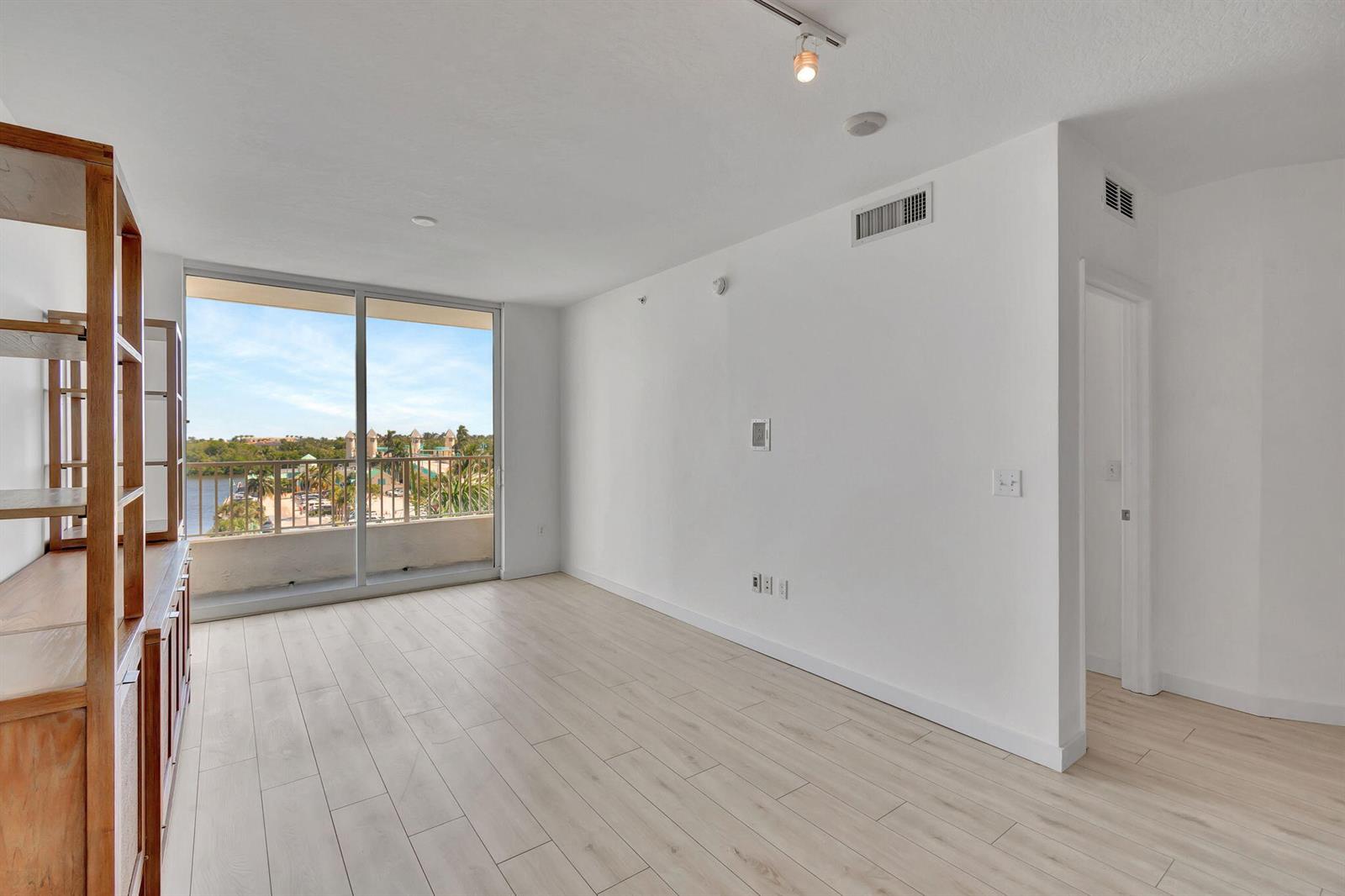 An empty room features light wood-look flooring, white walls, and a sliding glass door to a balcony — 100 NE 6th Street # 505, Boynton Beach FL 33435, BOYNTON BEACH, FL