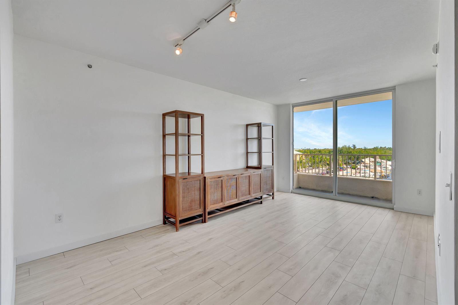 An empty living room features light wood flooring, a wooden wall unit, and a balcony view — 100 NE 6th Street # 505, Boynton Beach FL 33435, BOYNTON BEACH, FL