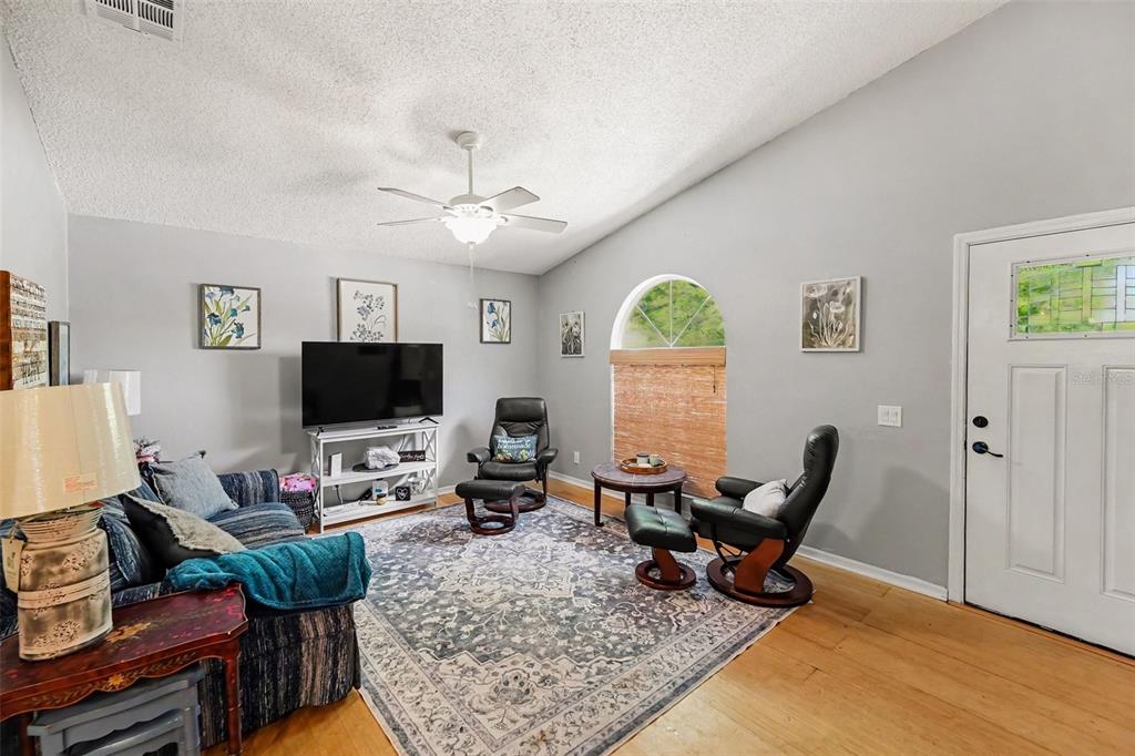 A living room with a vaulted ceiling, hardwood floors, a ceiling fan, and two recliners — 1934 29TH AVENUE N, ST PETERSBURG, FL