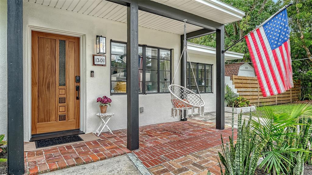 A front porch with a brick floor, a wooden door, and a hanging chair — 1301 6TH STREET W, PALMETTO, FL