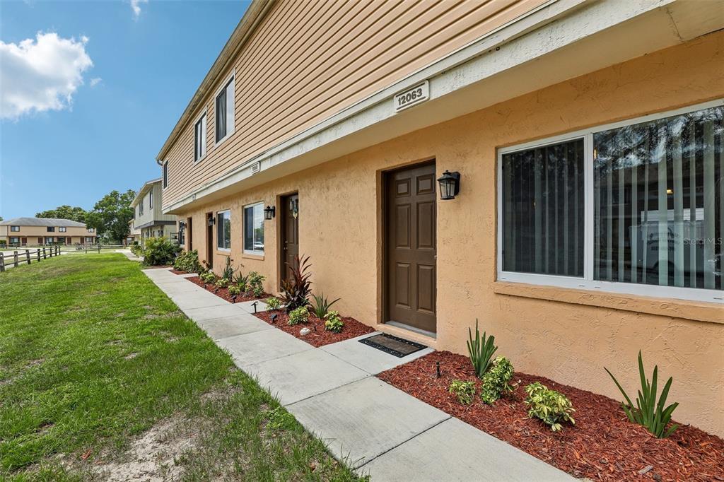 An exterior view of a two-story tan stucco townhouse with a concrete walkway and landscaping — 12057 TIFT CIRCLE, ORLANDO, FL