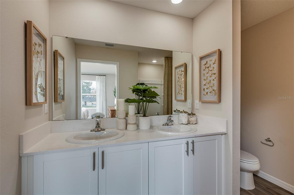A bathroom features a double vanity with white cabinets, a large mirror, and wall art — 4246 HILLOCK BOULEVARD, HAINES CITY, FL