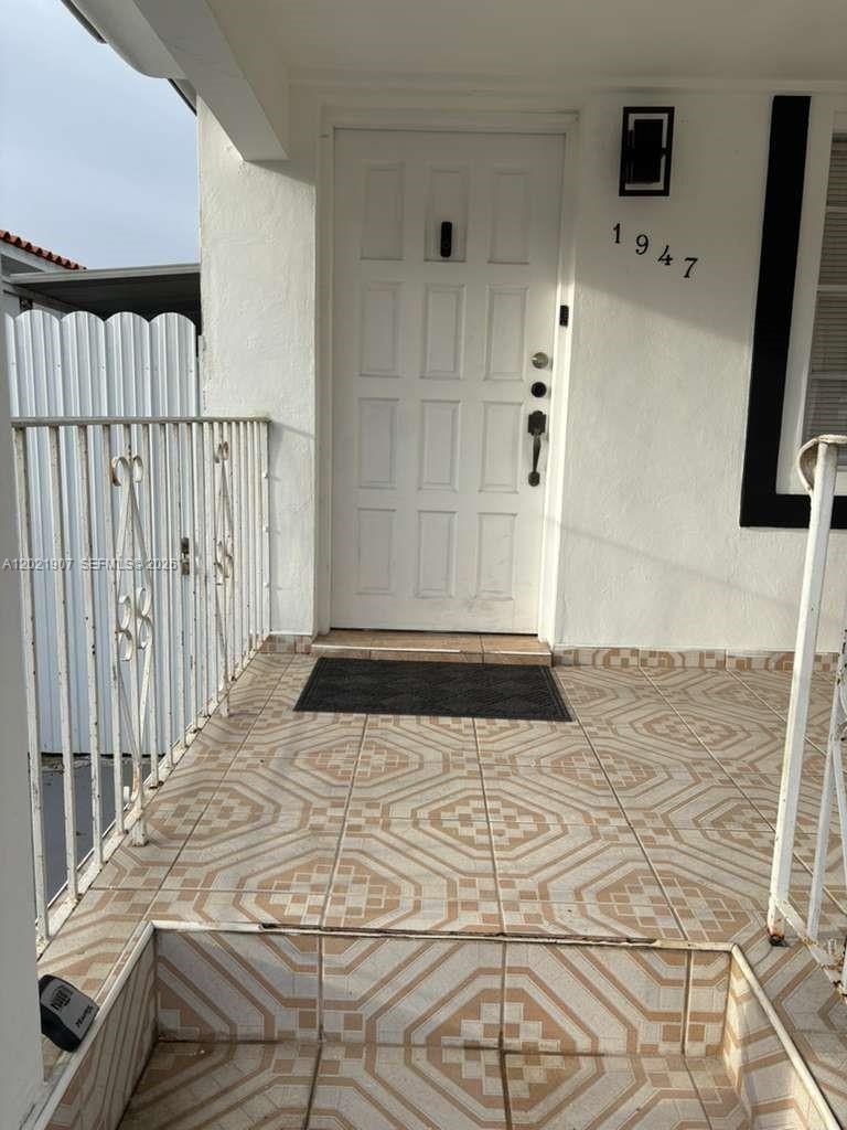 A white front door with a black handle sits on a tiled porch with railings — 1947 NW 33rd St # 1, Miami FL 33142, MIAMI, FL