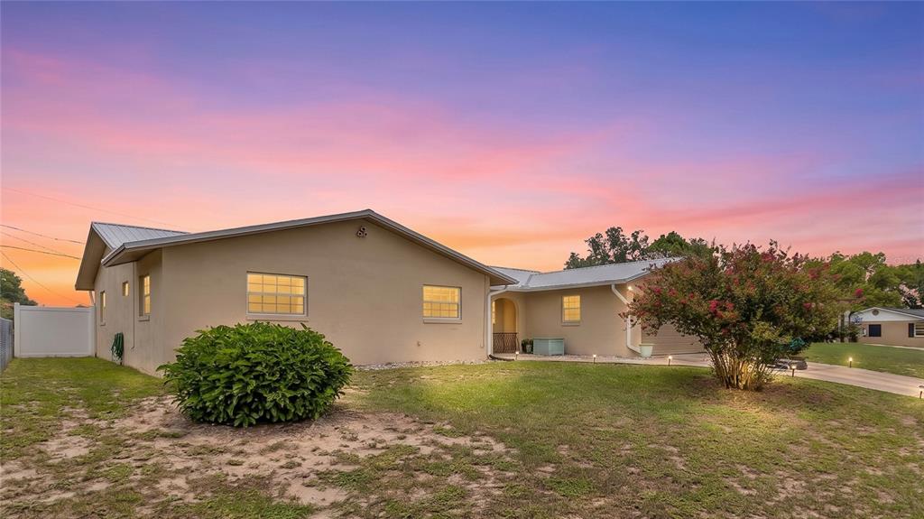 A single-story house with a beige exterior, metal roof, and a large bush in front — 1480 EDISON TERRACE, DELTONA, FL