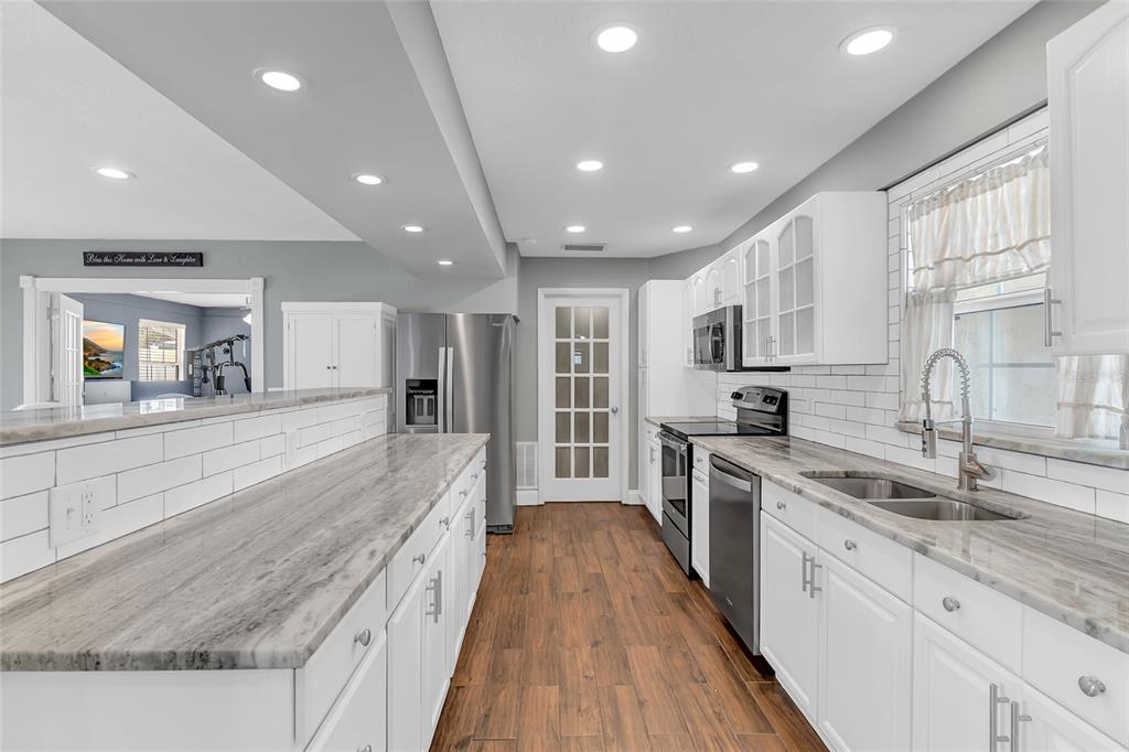 A kitchen features white cabinets, gray-veined countertops, a subway tile backsplash, and wood-look flooring — 1480 EDISON TERRACE, DELTONA, FL