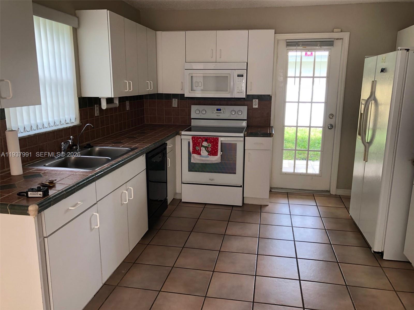 A kitchen features white cabinets, dark tile countertops, a black dishwasher, and tile flooring — 11274 SW 64 LN, Miami FL 33173, MIAMI, FL