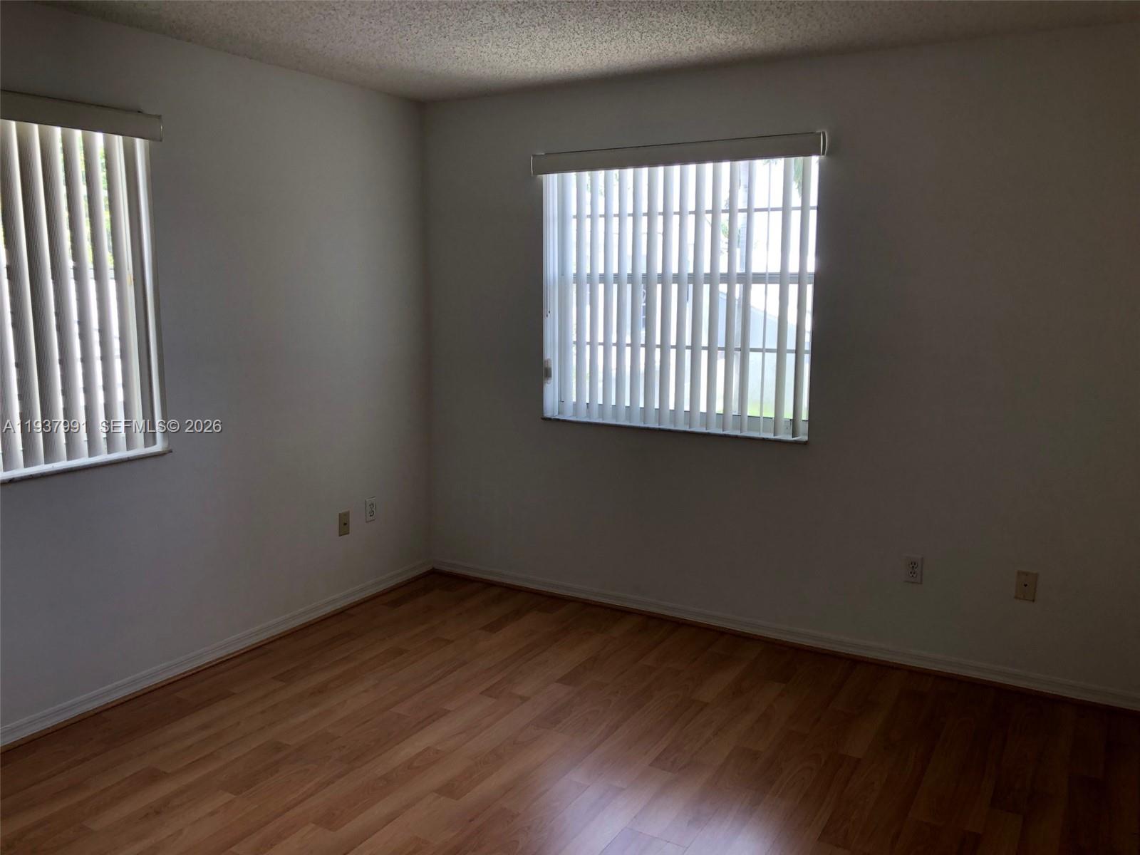 An empty room features light-colored walls, wood-look flooring, and two windows with vertical blinds — 11274 SW 64 LN, Miami FL 33173, MIAMI, FL