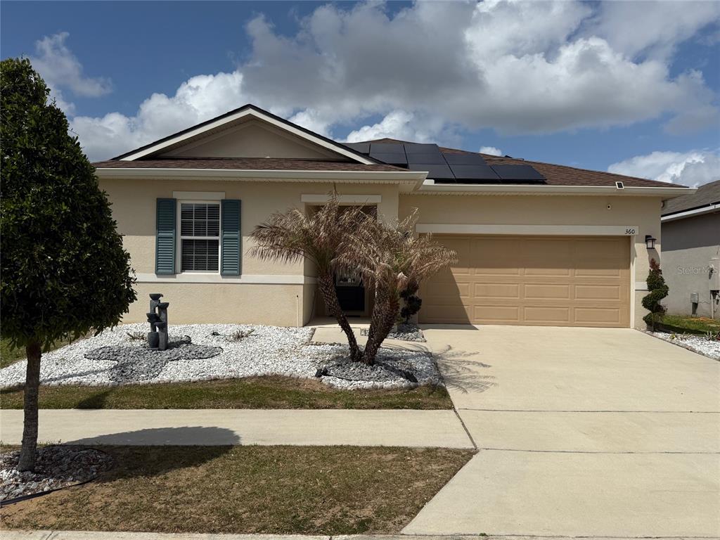 A single-story house with a beige stucco exterior, a two-car garage, and rooftop solar panels — 360 BUCHANNAN DRIVE, DAVENPORT, FL