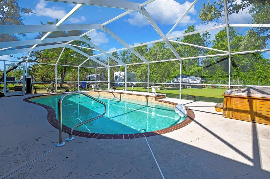 A screened-in swimming pool and hot tub on a concrete patio overlooking a grassy yard — 15157 DUCK HAWK ROAD, WEEKI WACHEE, FL