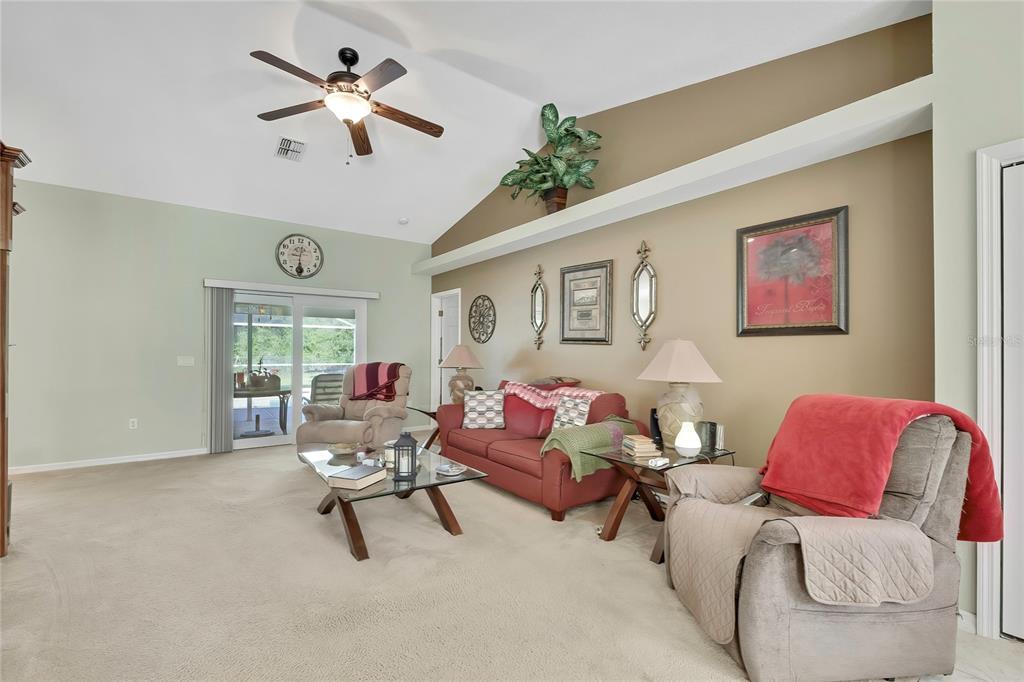 A living room features a vaulted ceiling, a ceiling fan, a red sofa, and recliners — 15157 DUCK HAWK ROAD, WEEKI WACHEE, FL