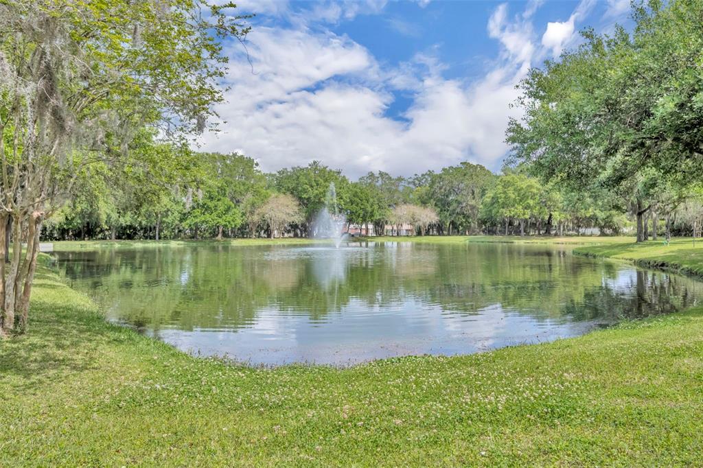 A pond with a central fountain is surrounded by green grass and mature trees — 1502 ASHDOWN COURT, SANFORD, FL