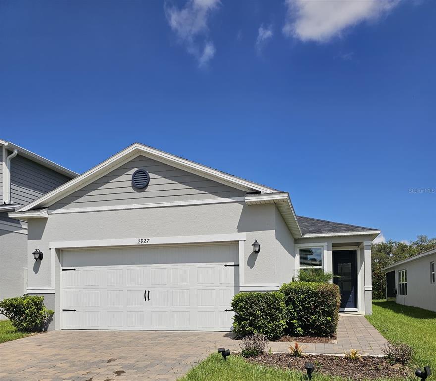 A single-story house with a light-colored stucco exterior, a two-car garage, and a paved driveway — 2927 SANCTUARY DRIVE, CLERMONT, FL