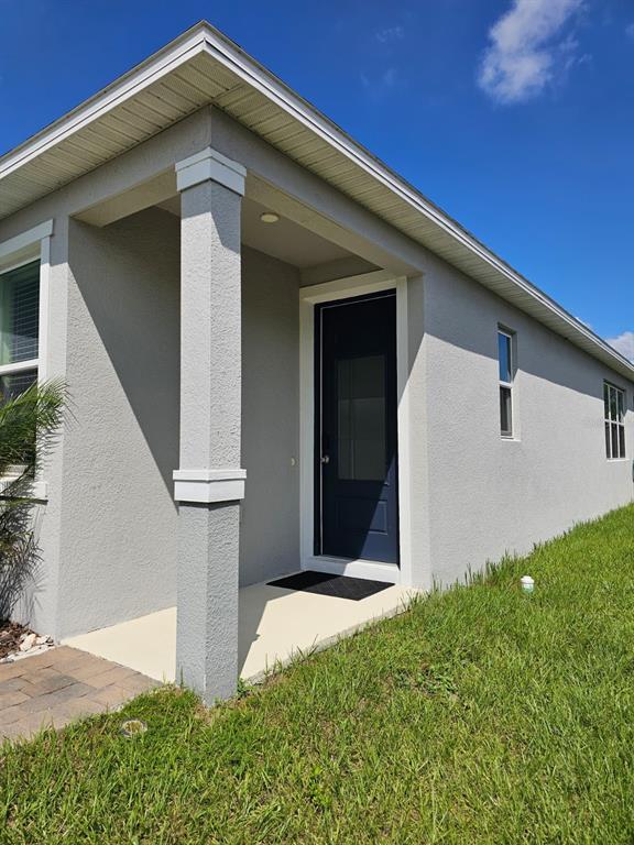A gray stucco house exterior features a covered entryway with a dark blue front door — 2927 SANCTUARY DRIVE, CLERMONT, FL