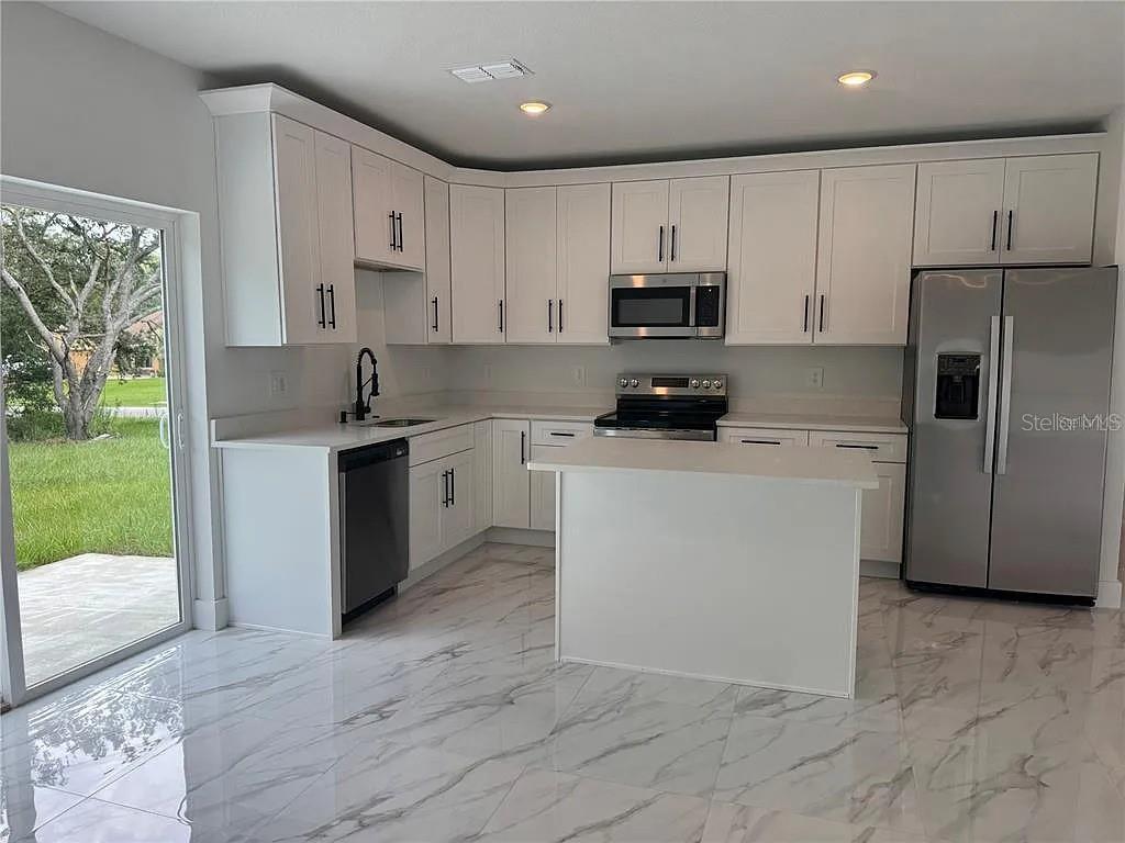 A modern kitchen features white cabinets, stainless steel appliances, and marble-patterned tile flooring — 2007 W HAMPSHIRE BOULEVARD, CITRUS SPRINGS, FL