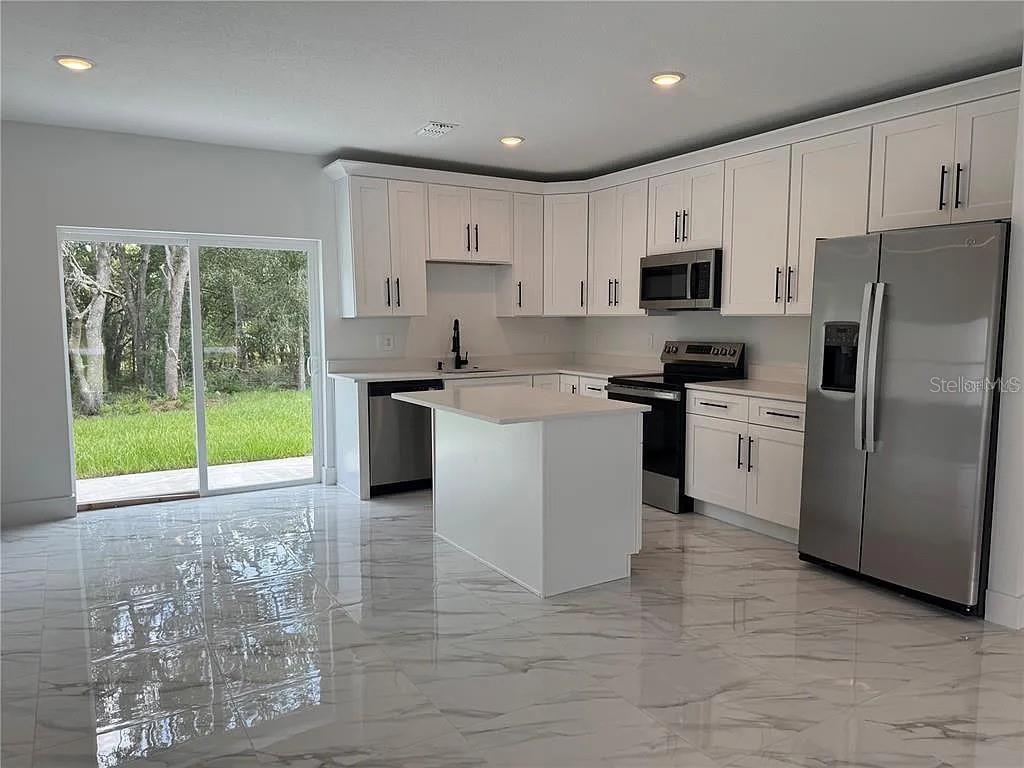 A modern kitchen features white cabinets, stainless steel appliances, a center island, and marble-look flooring — 2007 W HAMPSHIRE BOULEVARD, CITRUS SPRINGS, FL