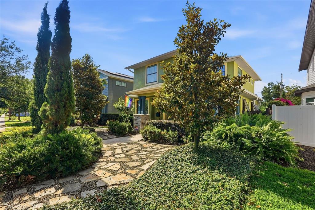 A two-story green house features a stone walkway, lush landscaping, and a pride flag — 2344 2ND AVENUE N, ST PETERSBURG, FL