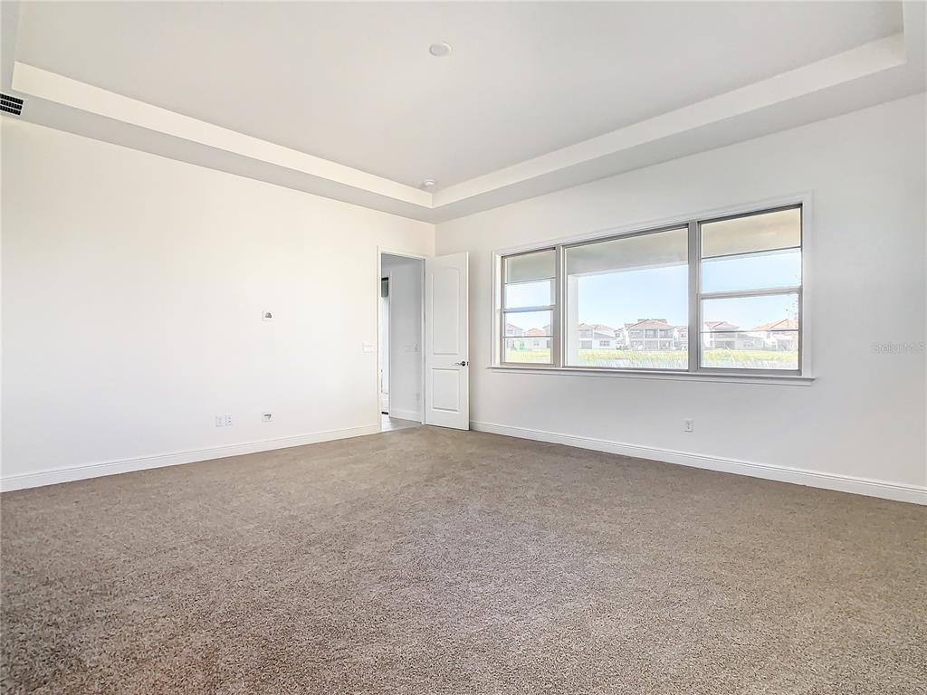 An empty bedroom features beige carpet, white walls, a tray ceiling, and a large window — 13899 LARKTON LANE, ORLANDO, FL