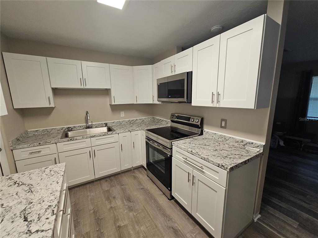 A kitchen features white cabinets, granite countertops, stainless steel appliances, and wood-look flooring — 114 MARRERO AVENUE, SEBRING, FL