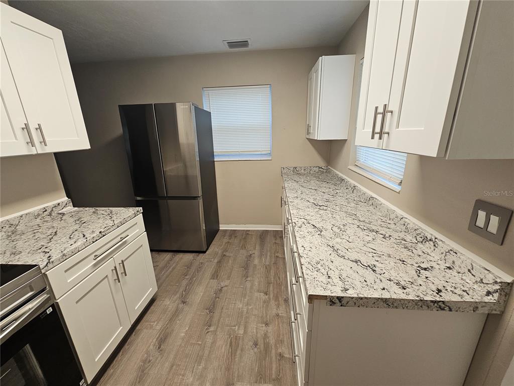 A kitchen features white cabinets, granite countertops, stainless steel appliances, and wood-look flooring — 114 MARRERO AVENUE, SEBRING, FL