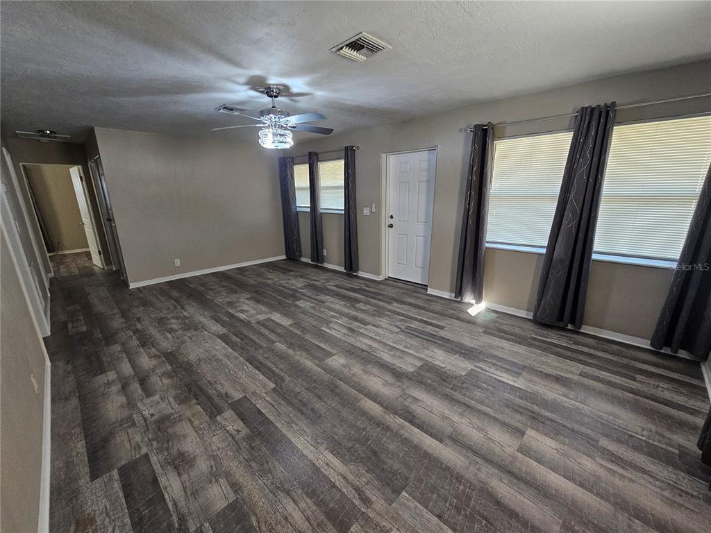An empty room features wood-look flooring, a ceiling fan, and windows with gray curtains — 114 MARRERO AVENUE, SEBRING, FL