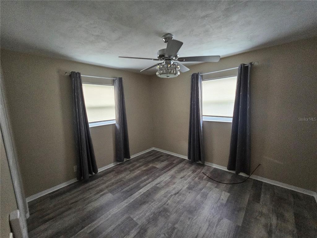 An empty bedroom features gray wood-look flooring, beige walls, two windows with curtains, and a fan — 114 MARRERO AVENUE, SEBRING, FL