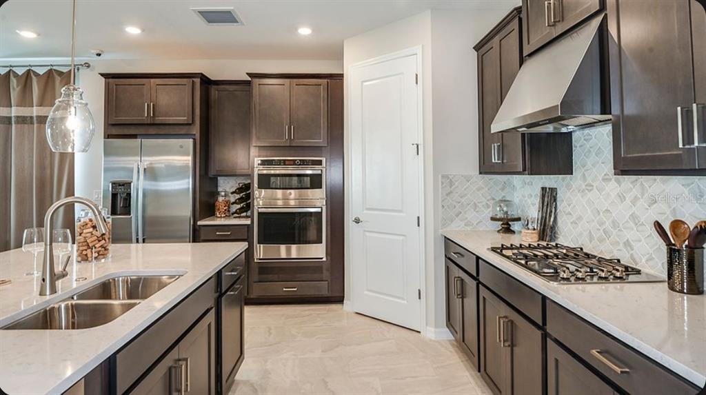 A modern kitchen features dark wood cabinets, stainless steel appliances, and a large center island — 1623 ANSON LANE, ZEPHYRHILLS, FL