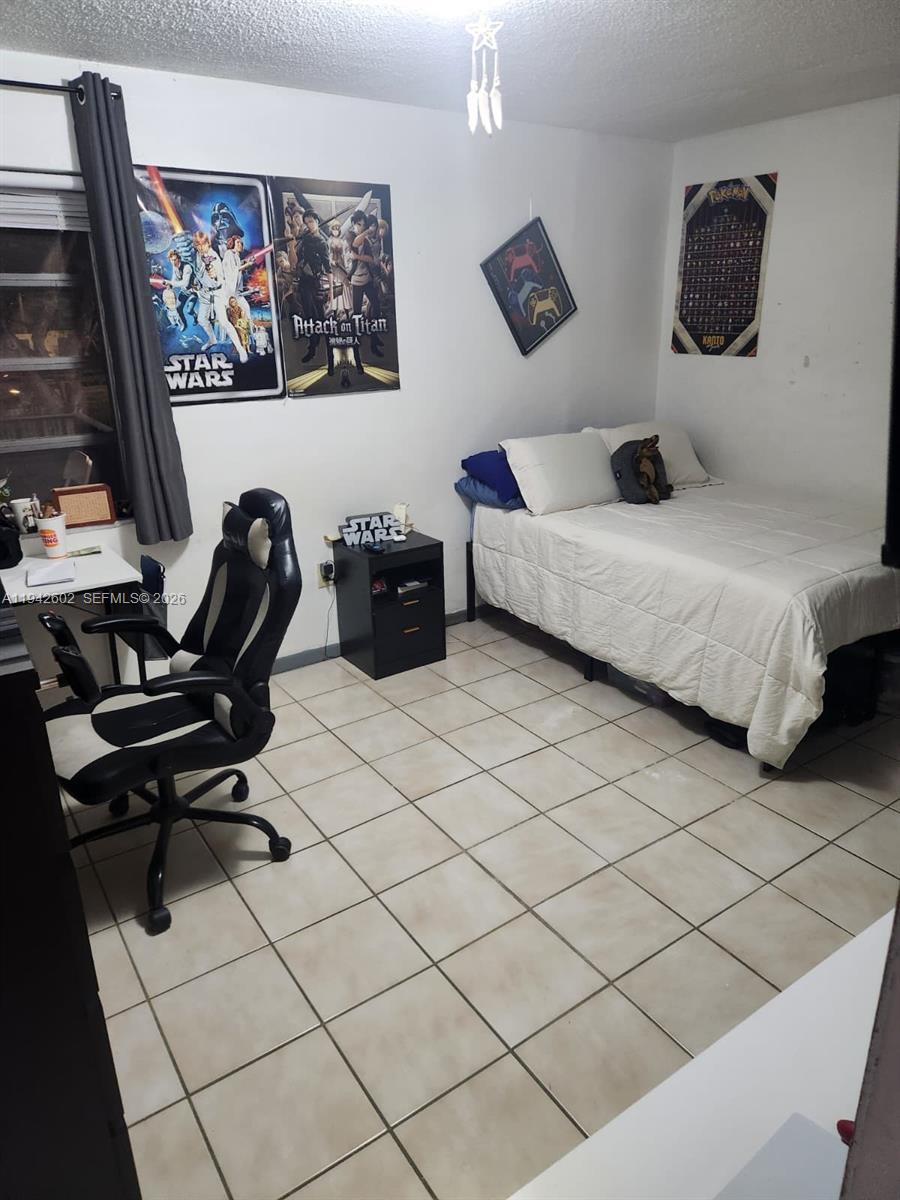 A bedroom with tile flooring, a bed, a desk with a gaming chair, and wall posters — 2498 SW 17th Ave # 4209, Miami FL 33145, MIAMI, FL