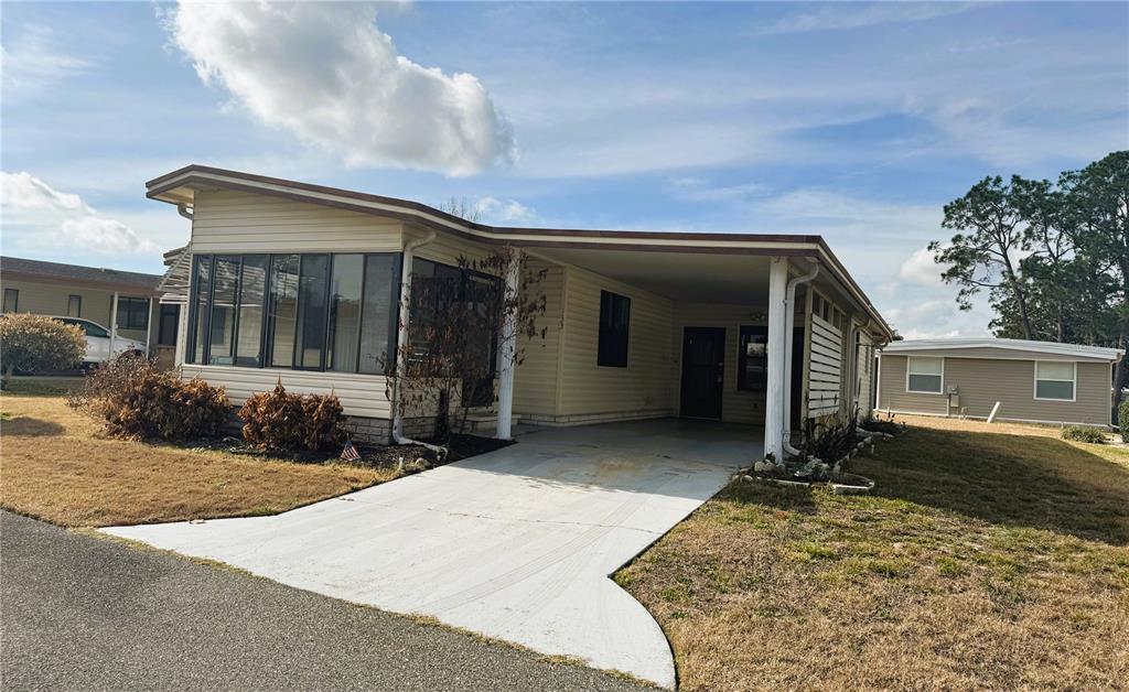 A single-story mobile home with a carport, a screened-in porch, and light-colored vinyl siding — 133 HIBISCUS WAY, LEESBURG, FL