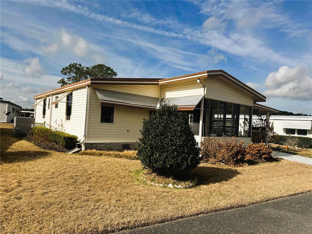 A light-colored manufactured home features a screened-in porch and a small front yard — 133 HIBISCUS WAY, LEESBURG, FL