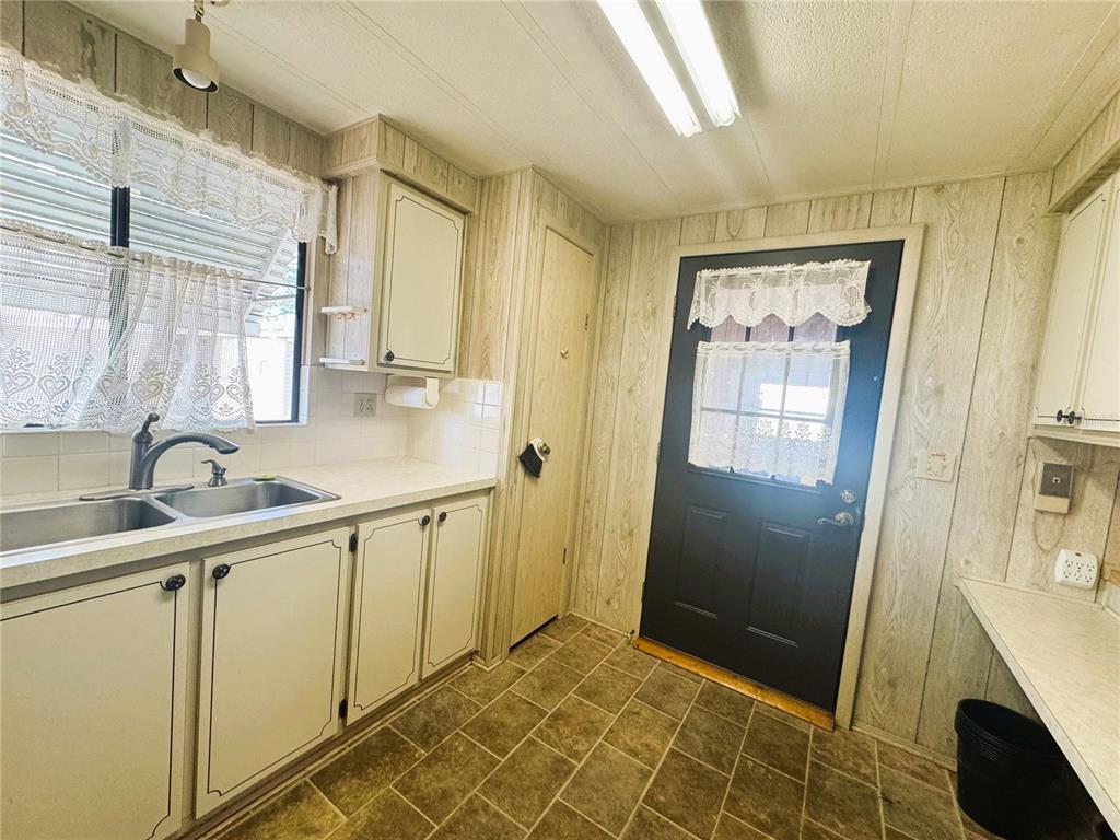 A kitchen features wood-paneled walls, white cabinets, a dark door, and a tiled floor — 133 HIBISCUS WAY, LEESBURG, FL