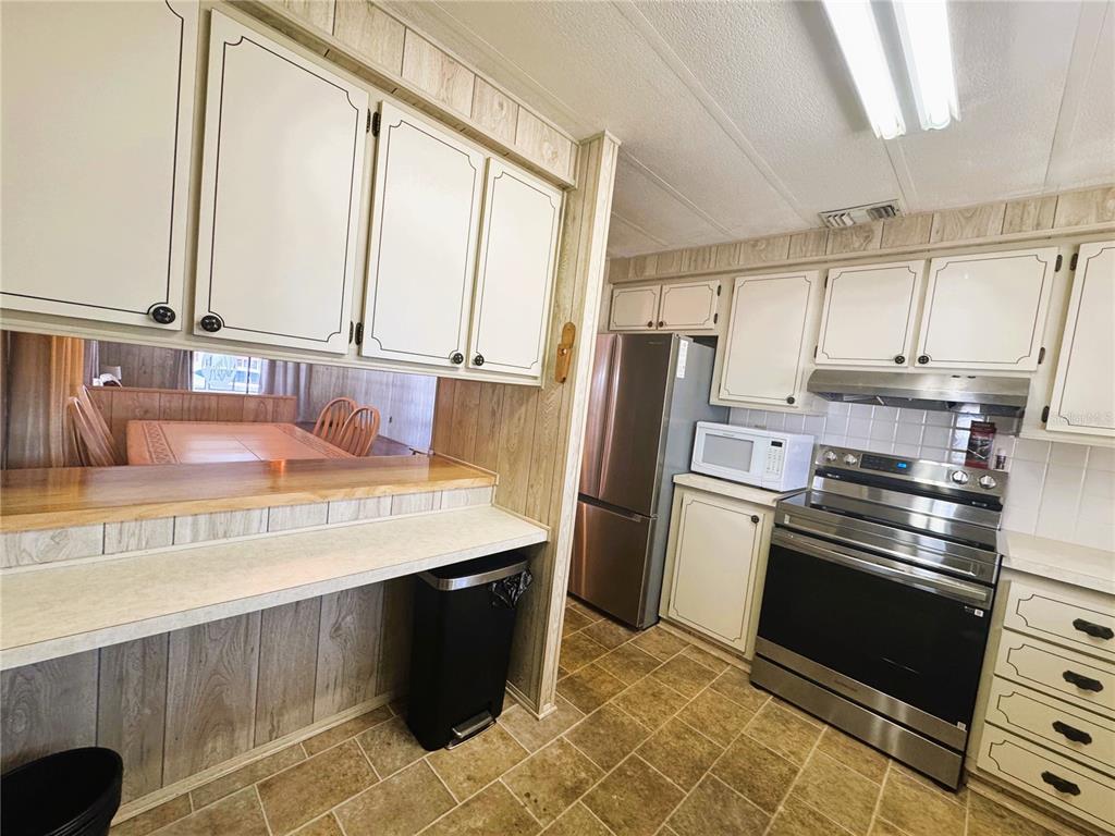 A kitchen with white cabinets, stainless steel appliances, and a wood-paneled breakfast bar — 133 HIBISCUS WAY, LEESBURG, FL