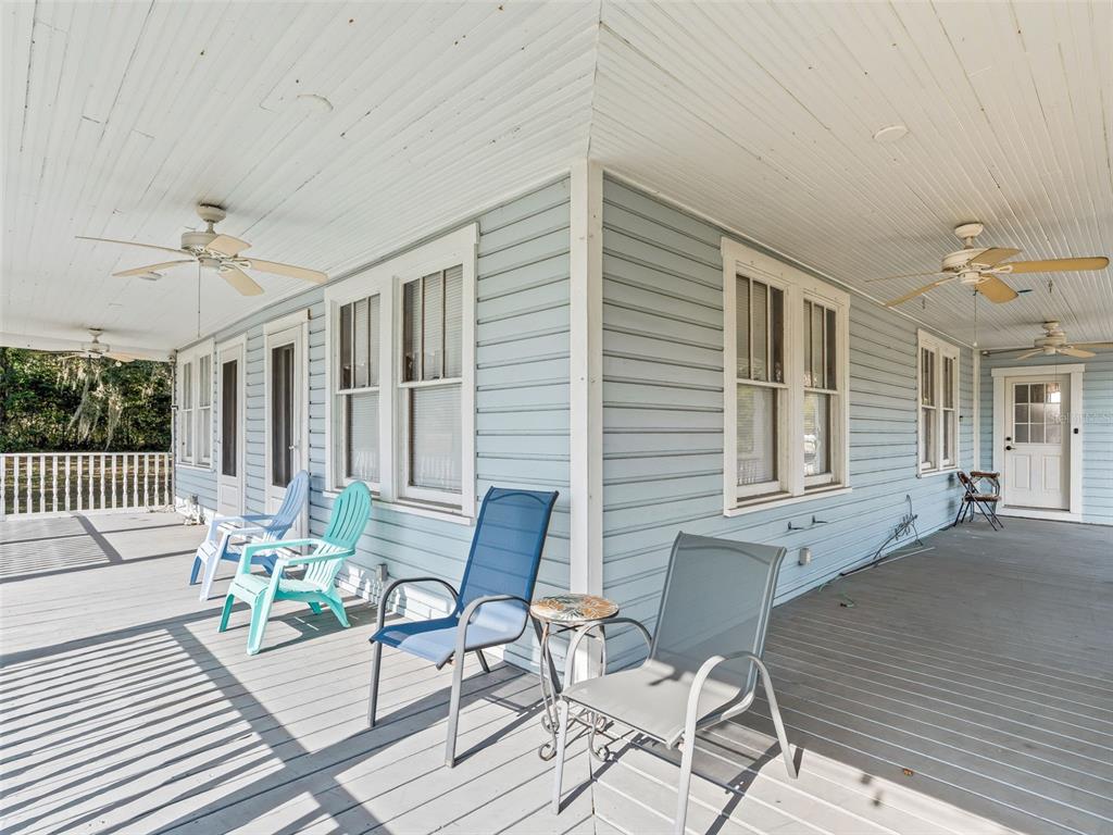 A wide, covered wrap-around porch features light blue siding, white trim, and several outdoor chairs — 10487 SE HIGHWAY 42, SUMMERFIELD, FL