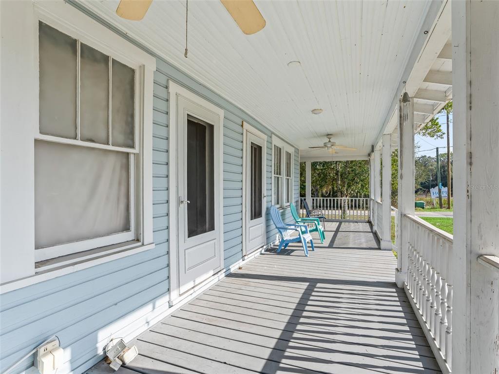 A covered porch features light blue siding, gray wooden decking, and several outdoor chairs — 10487 SE HIGHWAY 42, SUMMERFIELD, FL