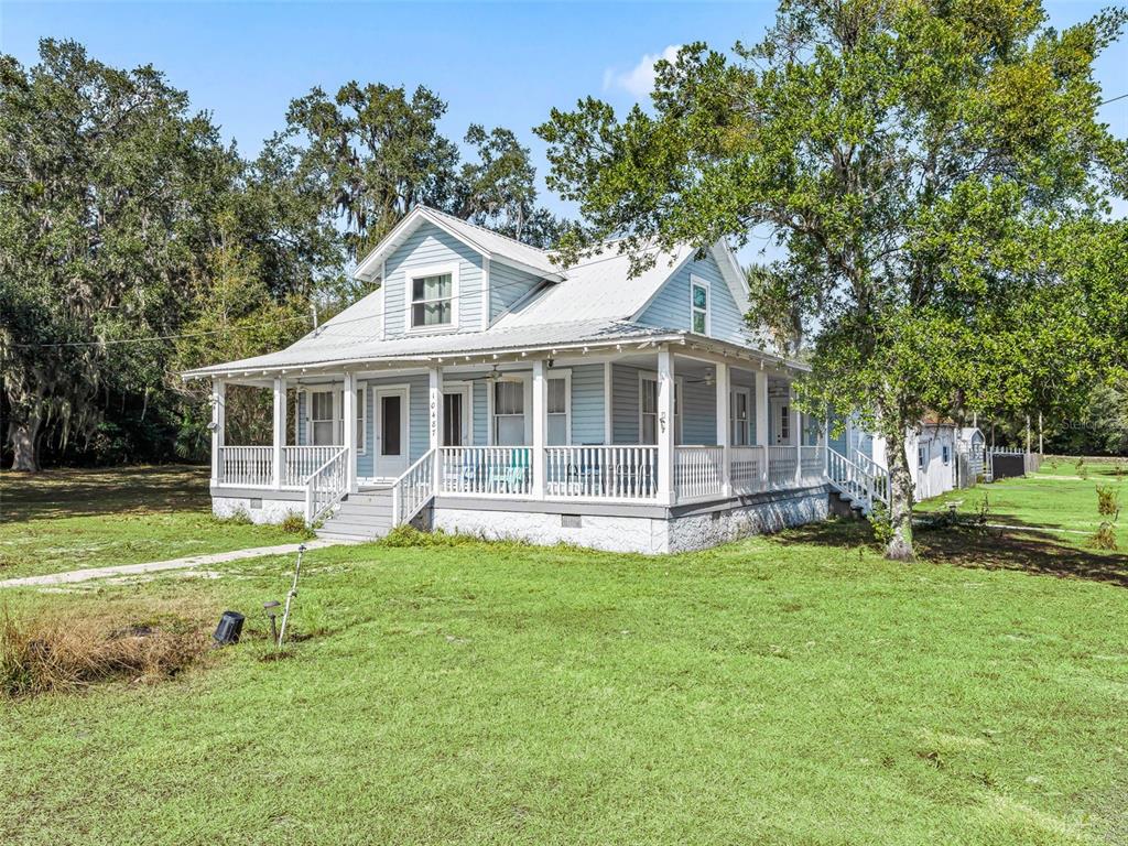 A light blue two-story house with a wrap-around porch sits on a grassy lot — 10487 SE HIGHWAY 42, SUMMERFIELD, FL