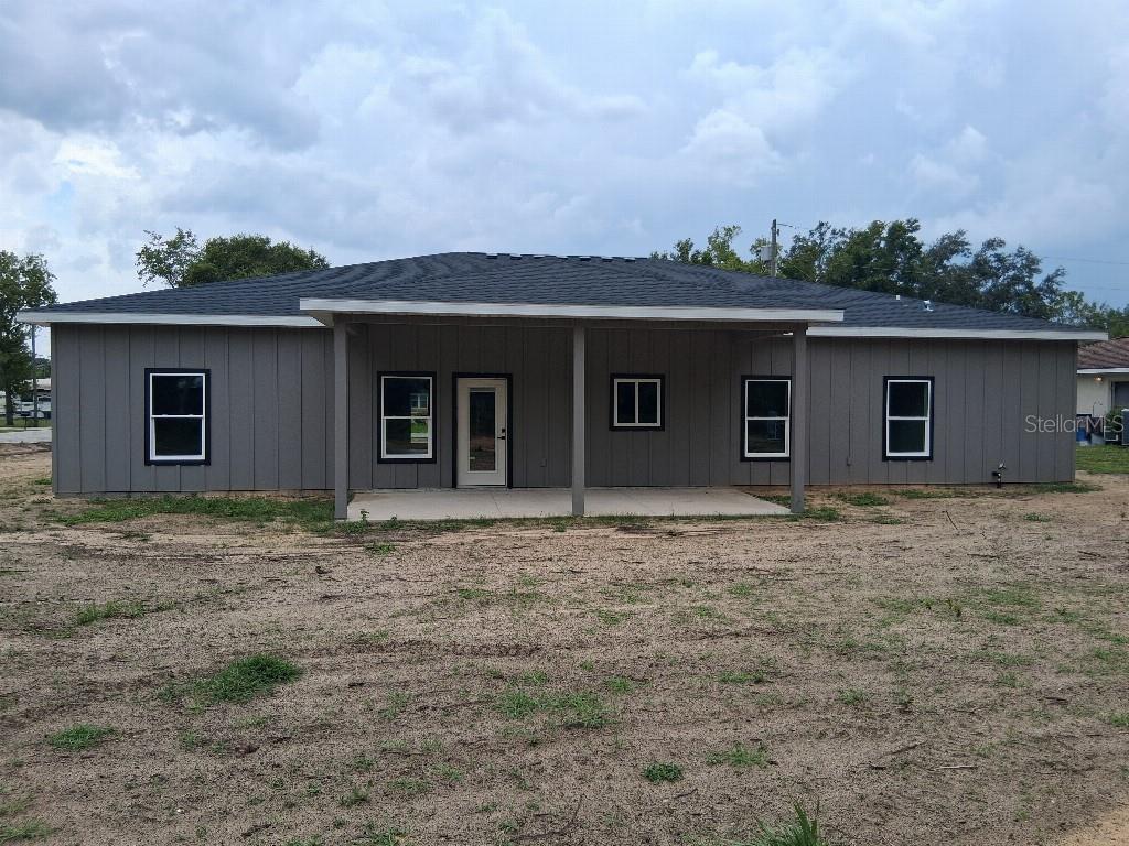 The exterior of a gray, single-story house features a covered concrete patio and dark-trimmed windows — 9469 SE 154TH STREET, SUMMERFIELD, FL