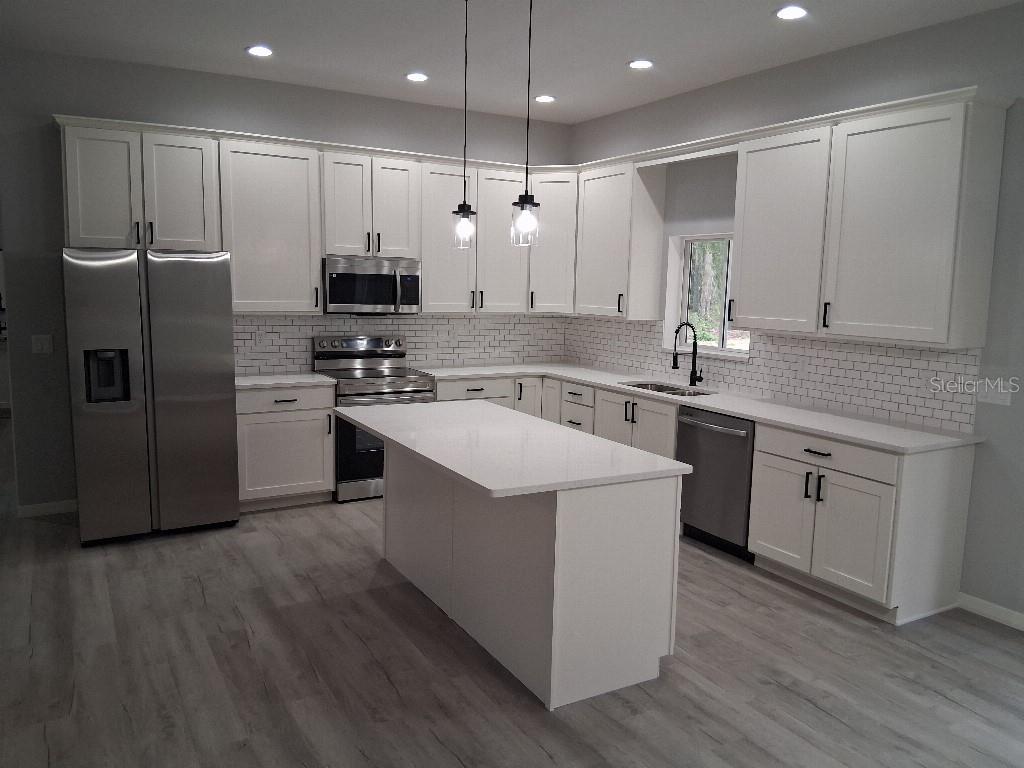 A modern kitchen features white cabinets, stainless steel appliances, a central island, and subway tile — 9469 SE 154TH STREET, SUMMERFIELD, FL