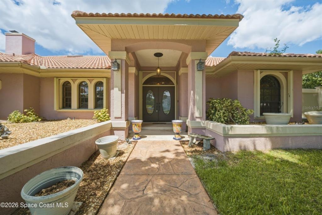 The exterior of a house features a covered entryway with double doors and arched windows — 4562 HELENA DRIVE, TITUSVILLE, FL