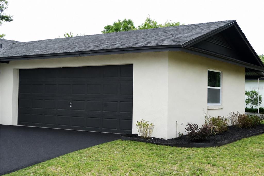 A side view of a house exterior featuring a black garage door and asphalt driveway — 3202 TRADEWINDS TRAIL, ORLANDO, FL