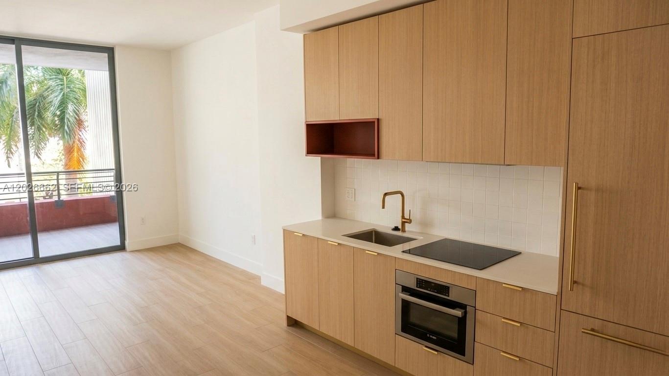 A modern kitchen features light wood cabinets, a white tile backsplash, and a glass balcony door — 90 NE 32nd St. # 209, Miami FL 33137, MIAMI, FL