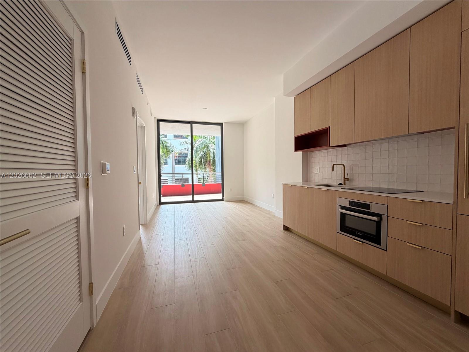 A modern kitchen with light wood cabinets and a balcony view through sliding glass doors — 90 NE 32nd St. # 209, Miami FL 33137, MIAMI, FL