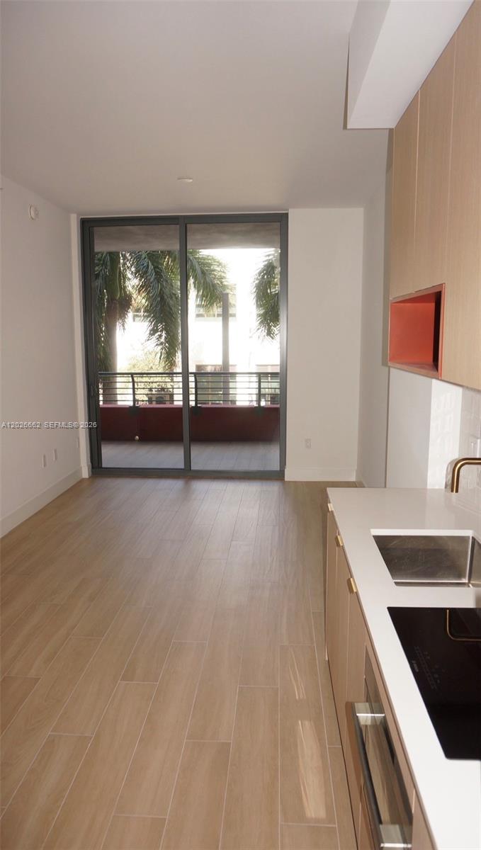 A modern kitchen area with light wood cabinets and tile flooring opens to a balcony — 90 NE 32nd St. # 209, Miami FL 33137, MIAMI, FL