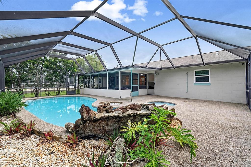 A screened-in pool area features a rock waterfall, a small spa, and a concrete patio — 2448 S DAYTONA AVENUE, FLAGLER BEACH, FL