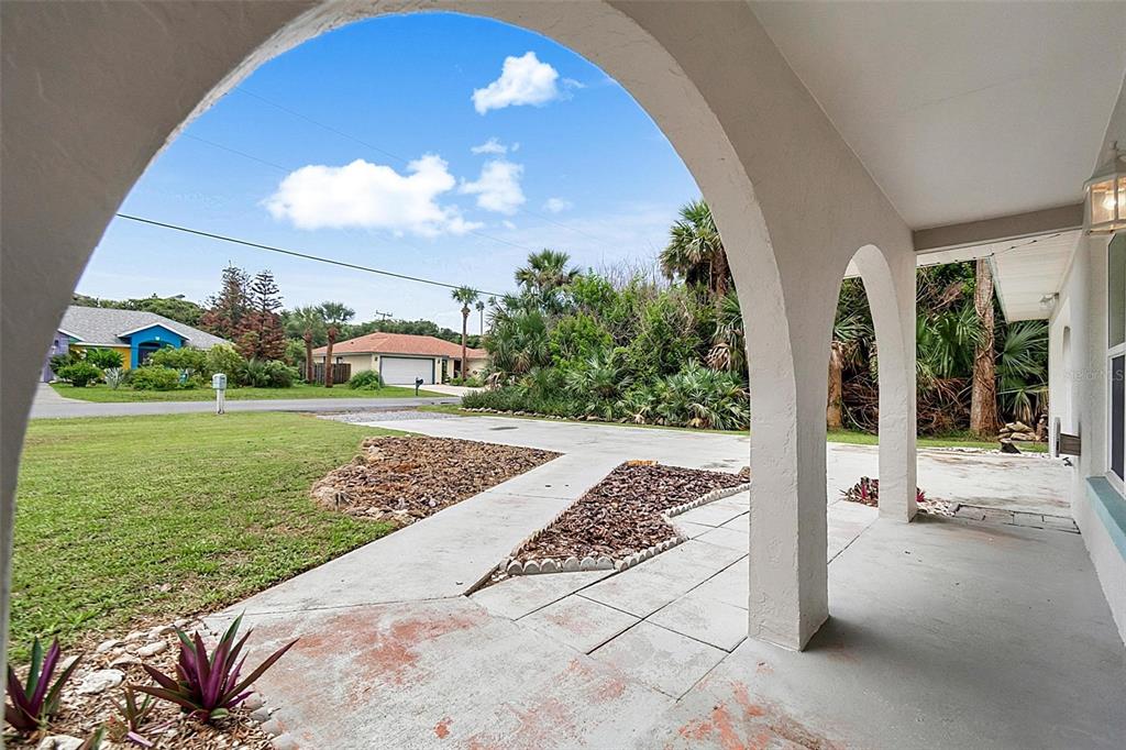 A covered porch with arched openings overlooks a driveway, lawn, and neighboring houses — 2448 S DAYTONA AVENUE, FLAGLER BEACH, FL