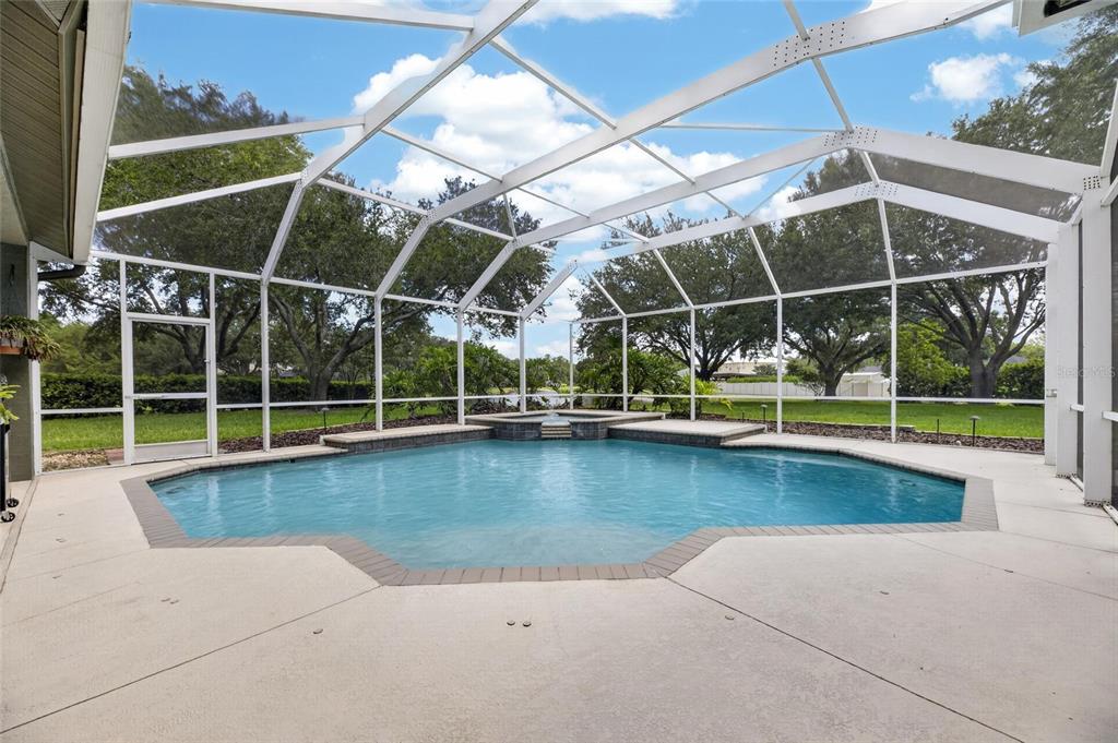 A screened-in swimming pool and spa with a concrete deck under a white frame enclosure — 7508 DUNBRIDGE DRIVE, ODESSA, FL