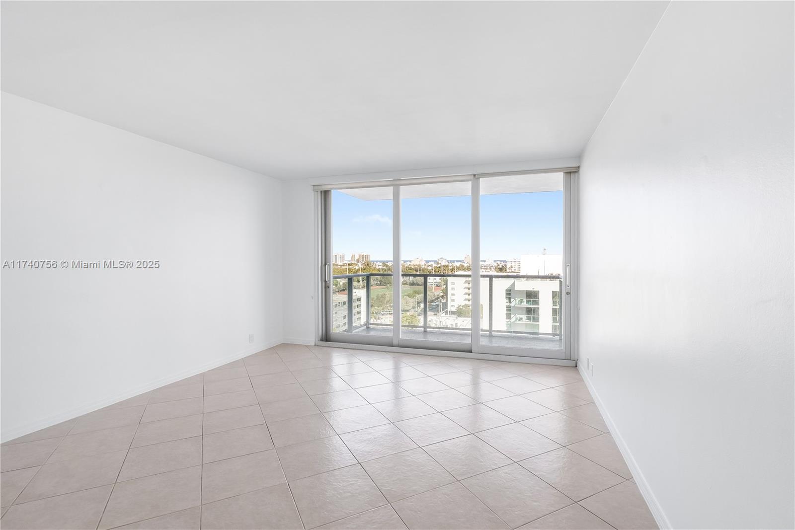 An empty room features white walls, beige tile flooring, and a sliding glass door to a balcony — 1000 West Ave # 1008, Miami Beach FL 33139, MIAMI BEACH, FL
